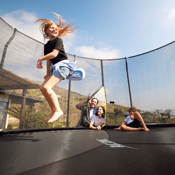 Child jumping on a trampoline with adults watching outdoors.