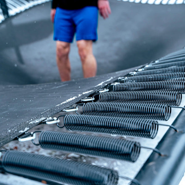 Close-up of trampoline springs with a person wearing blue shorts in the background