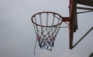 Outdoor basketball hoop with a red, white, and blue net against a cloudy sky