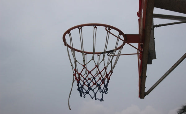 Outdoor basketball hoop with a red, white, and blue net against a cloudy sky