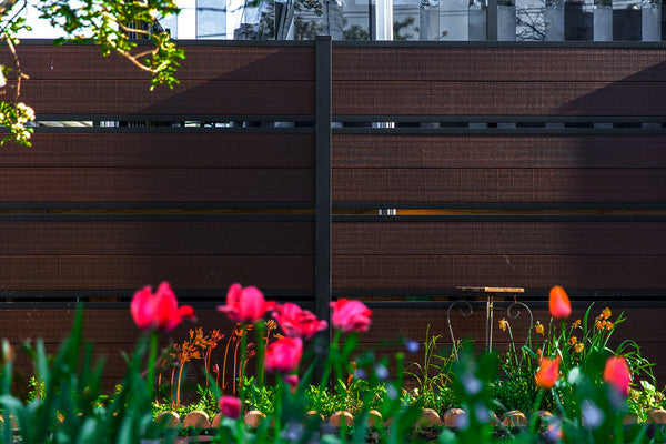 Dark brown horizontal slat privacy fence behind a garden bed of red tulips