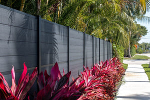 Charcoal horizontal composite privacy fence running along a landscaped walkway with tropical plantings