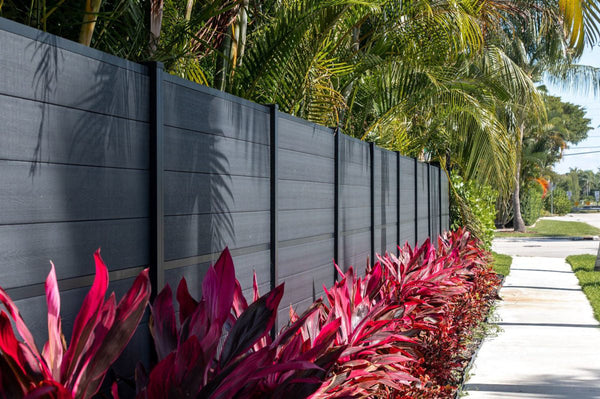 Charcoal horizontal composite privacy fence running along a landscaped walkway with tropical plantings