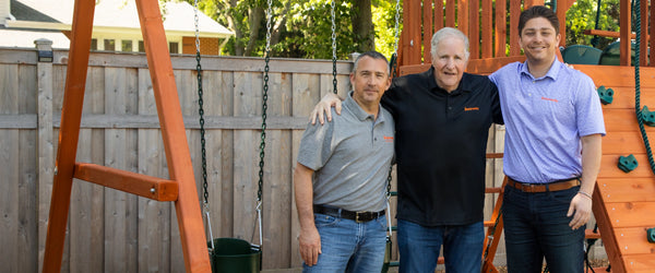 Three generations of the Fenceworks family in front of a wooden swing set