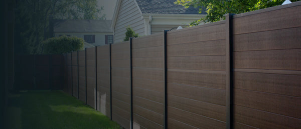 Dark brown composite privacy fence enclosing a backyard lawn