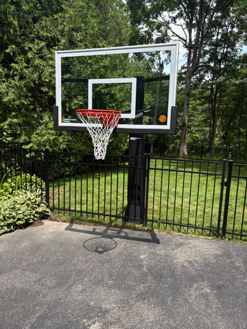 In-ground basketball hoop installed on a residential driveway behind a black aluminum fence