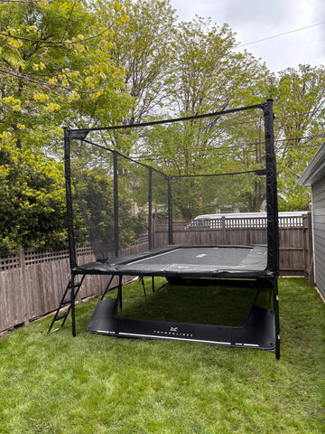 Black rectangular ACON trampoline with safety enclosure net installed in a backyard