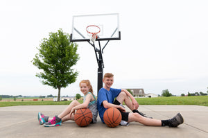 Two Kids Sitting in front of a Basketball Hoop, the Proview basketball hoop system