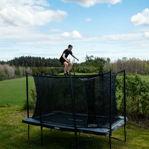 Person jumping on a NORTH Legend rectangular trampoline with a safety enclosure in a grassy yard