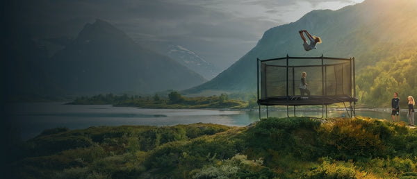 A trampoline with a safety enclosure on a hillside overlooking a lake and mountains