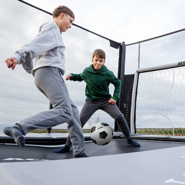 Two children playing with a soccer ball on an indoor trampoline.