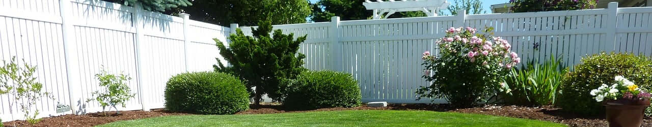White vinyl privacy and picket fence in a landscaped backyard with shrubs and roses