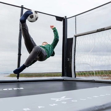 Person playing soccer on a trampoline with a goal in the background