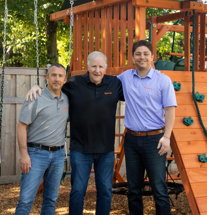 Three generations of the Fenceworks family in front of a wooden swing set