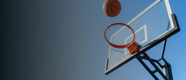 A basketball dropping through the net of an outdoor hoop against a blue sky