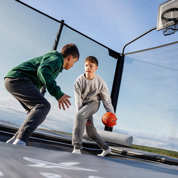 Two children playing basketball on a trampoline 