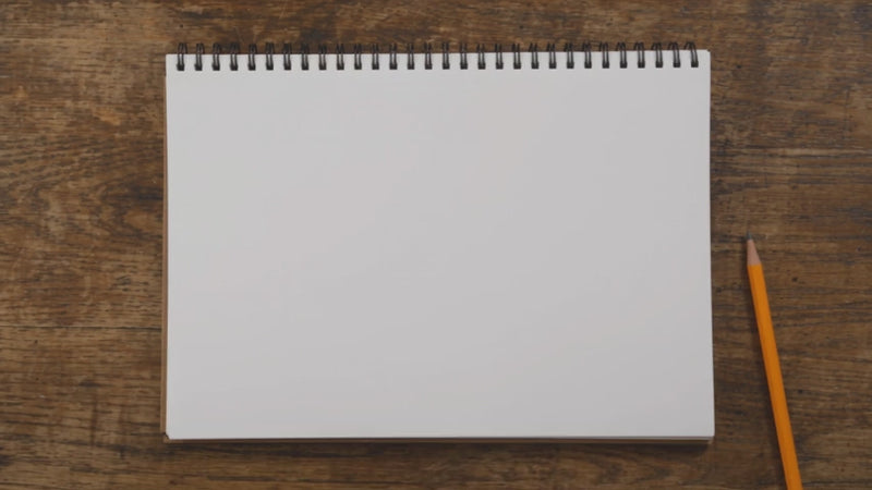 A blank sketchpad and pencil on a wooden table