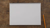 A blank sketchpad and pencil on a wooden table