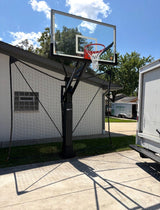 Safety net ball containment system installed behind an in-ground basketball hoop beside a driveway